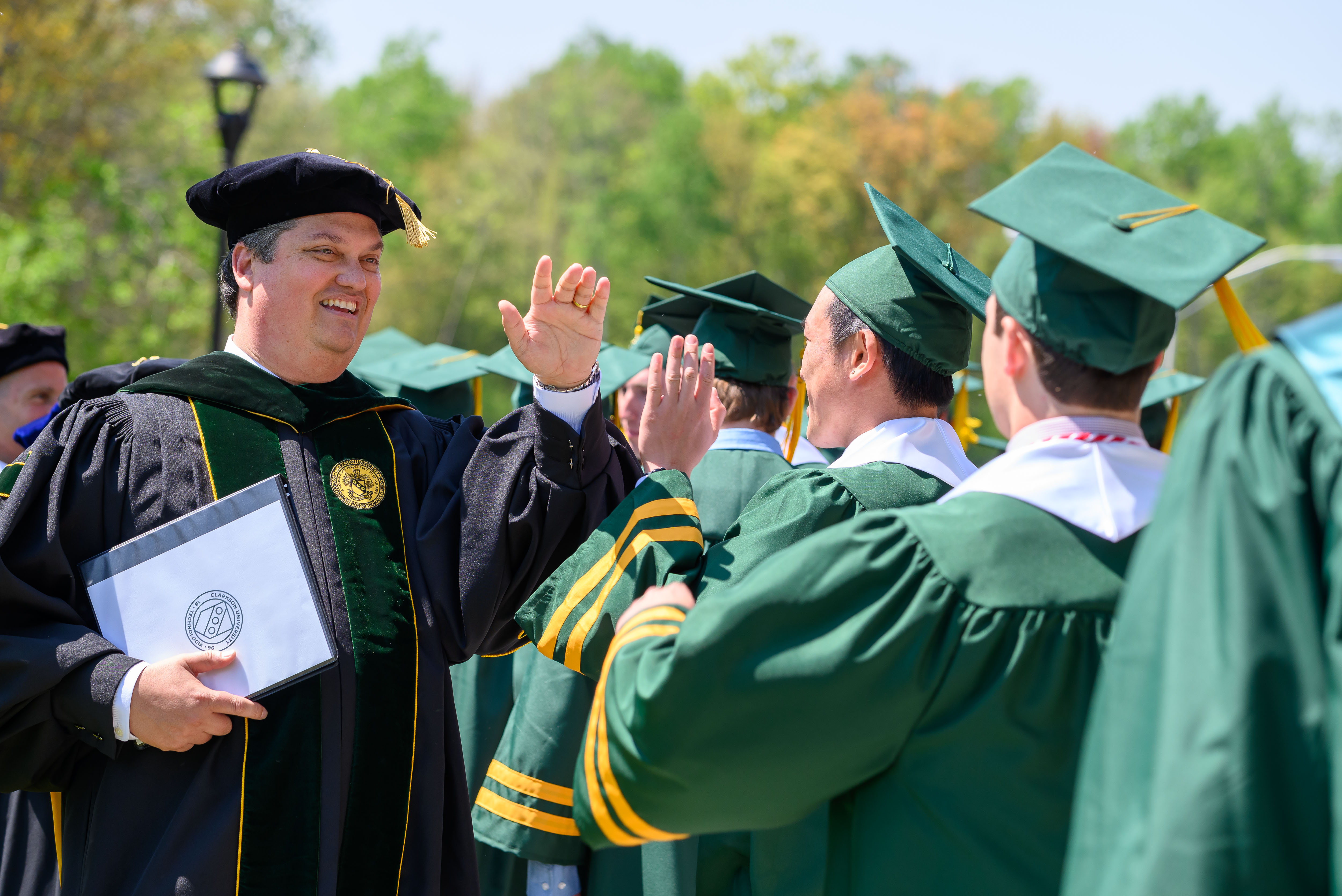 Clarkson President Marc Christensen high fives students during Commencement.