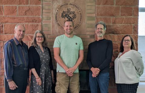 a group of five professors posing in front of a sandstone wall with the Clarkson seal