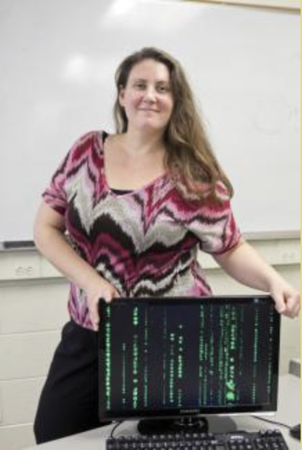 Girl standing next to a computer with board behind her