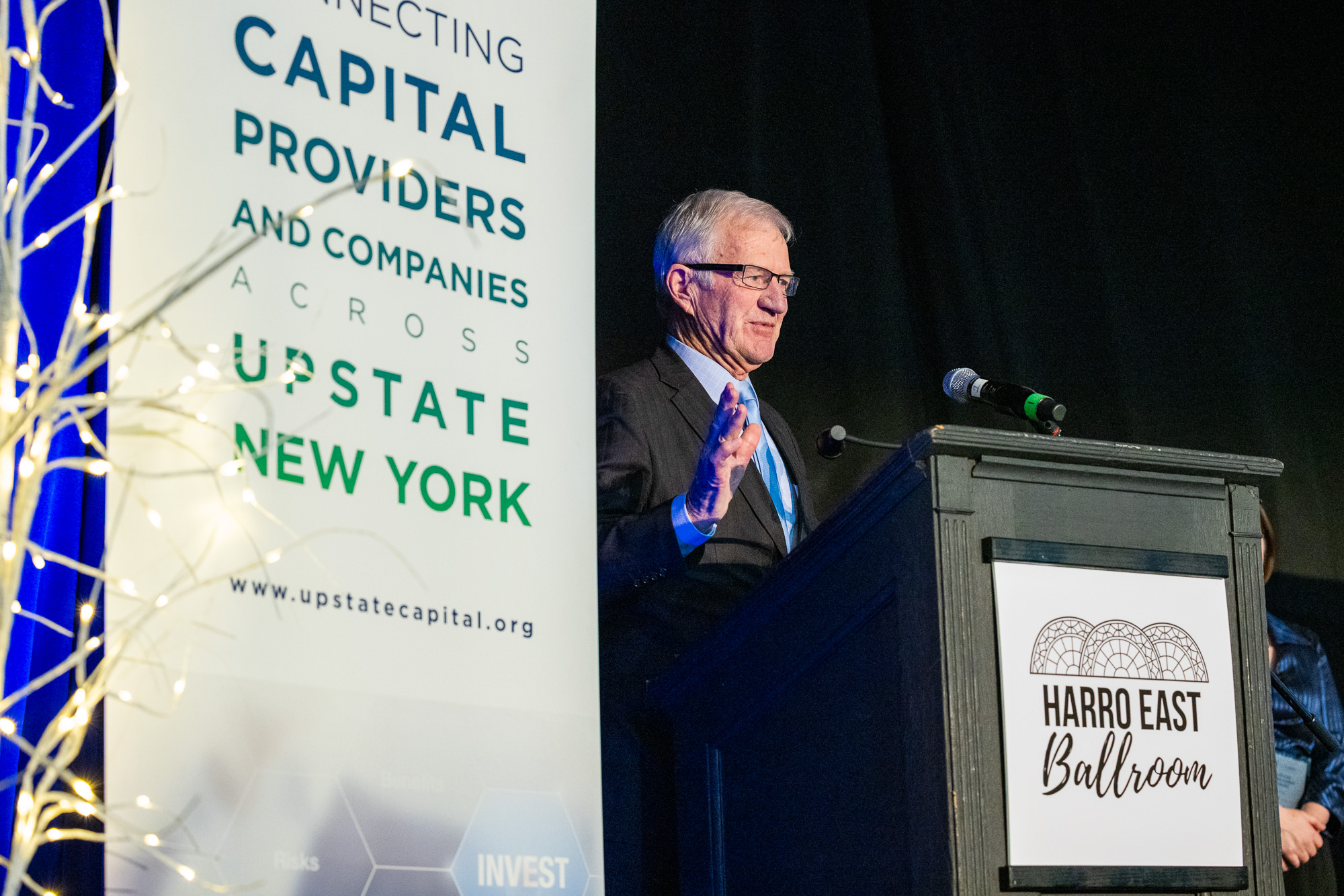 Former Clarkson University President Tony Collins stands on stage to accept Lifetime  Achievement Award from Upstate Capital Association of New York