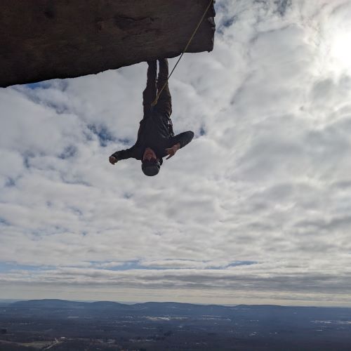 A photo of Carson Bruening hanging upside down on a climbing trip.