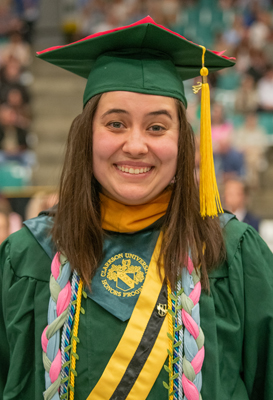 Chest-up photo of Celia Darling in green and gold commencement regalia and green mortarboard hat.