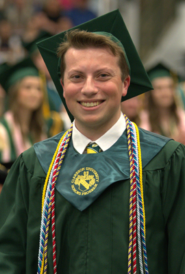 Chest-up photo of Miles Compani in green and gold commencement regalia with green mortarboard hat
