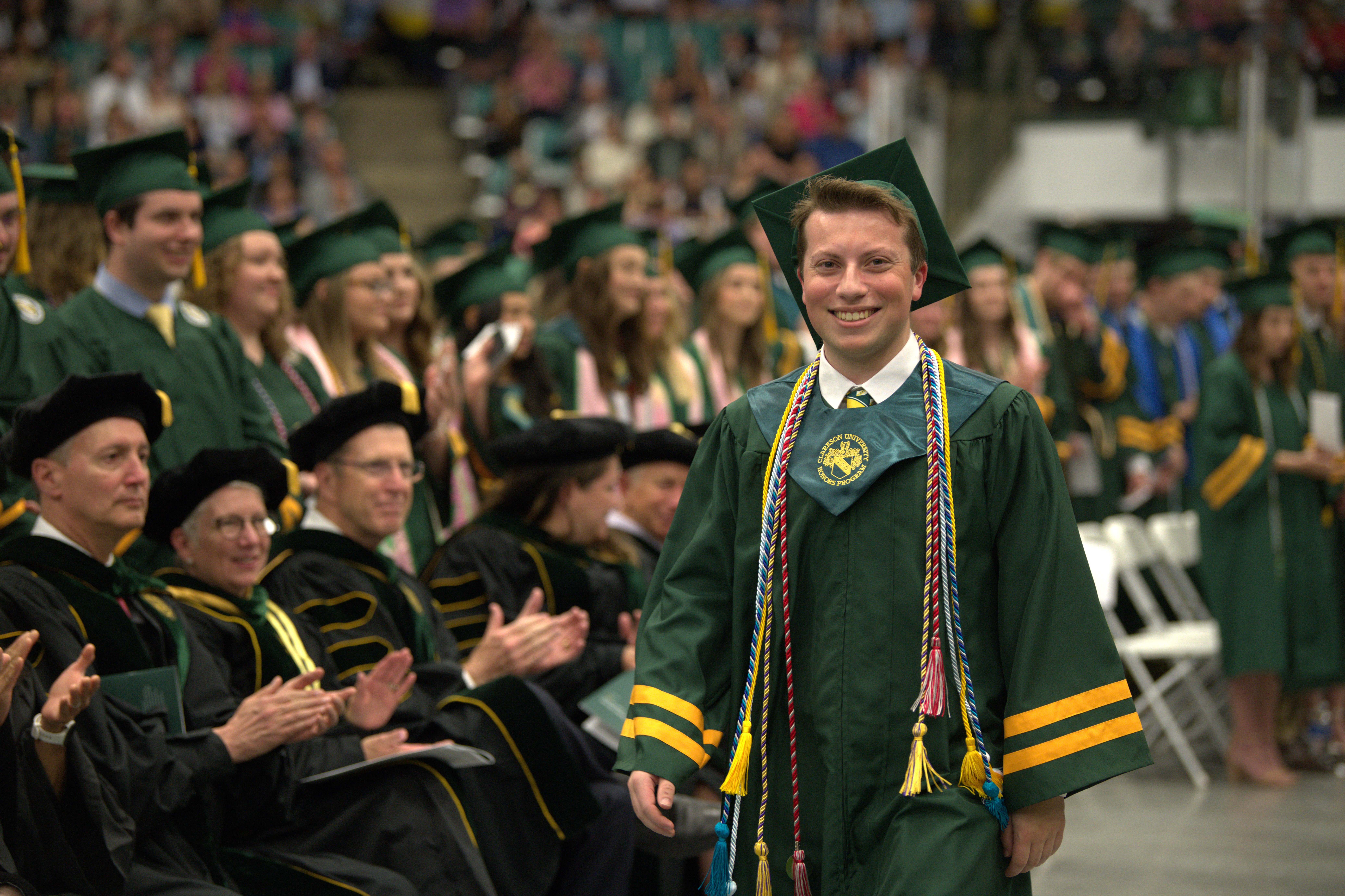 A student in regalia smiles as he walks past peers at commencement.