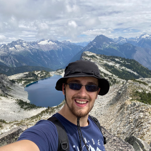 A photo of Sam Carusone on top of a mountain surrounding a lake.