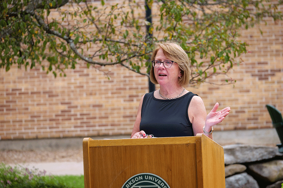 Patricia Darnell stands at a podium outside and talks about Ronald Wells '68.
