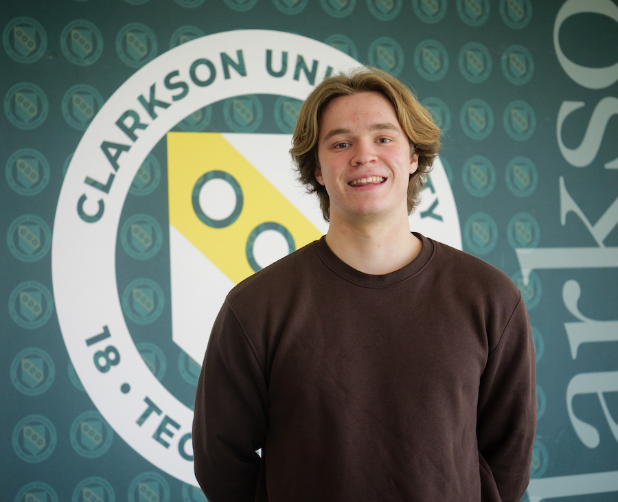 Mark standing with the clarkson logo behind him on the wall