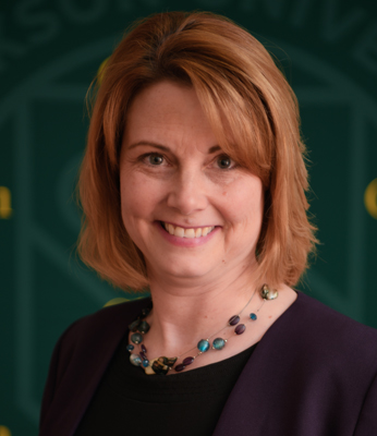 Shoulders-up portrait of Stacey Zeigler in a purple jacket and black shirt