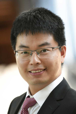 Shoulders up portrait of Suguang Xiao in black suit coat and red tie with white dots