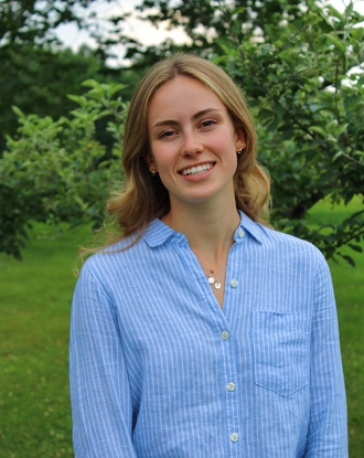 A photo of Emelyn Sullivan Smiling in front of a bush.