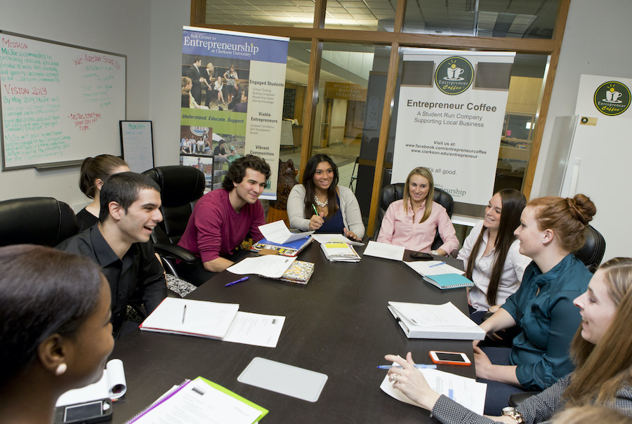 A group of students sit around a table while holding notepads and pencils.