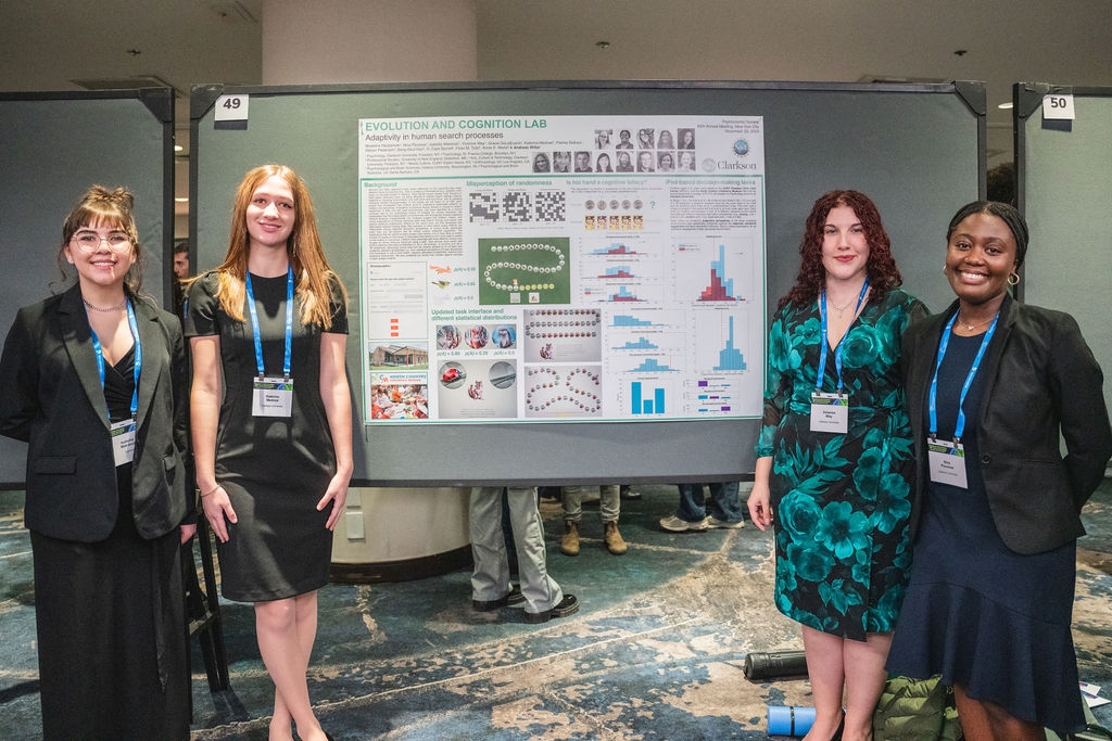 Four female students pose on either side of a large academic poster.