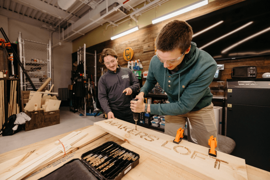 Guy drilling out the lettering for Maker's Loft with the assistance of a maker mentor