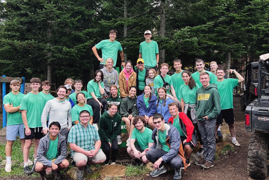 A group of students, wearing green t-shirts, smile and stand together.