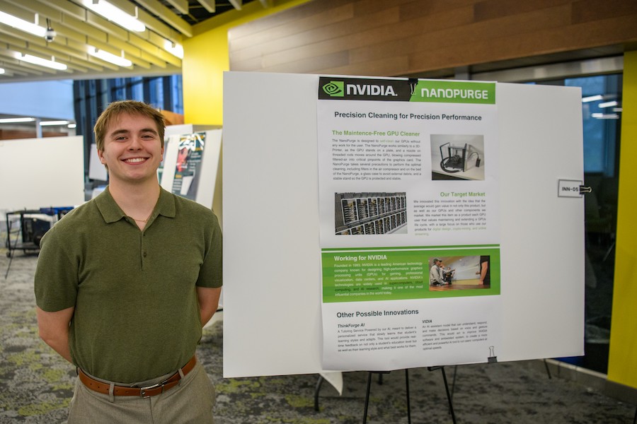 A male student smiles while standing in front of a poster describing a project.