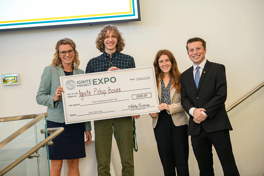 Clarkson Ignite director Ashley Sweeney poses with three students, including one who is holding up a large fake check for winning an award during the Ignite Project Expo