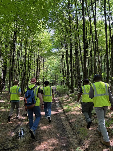 Students in high-vis vests walk through the woods on a dirt trail