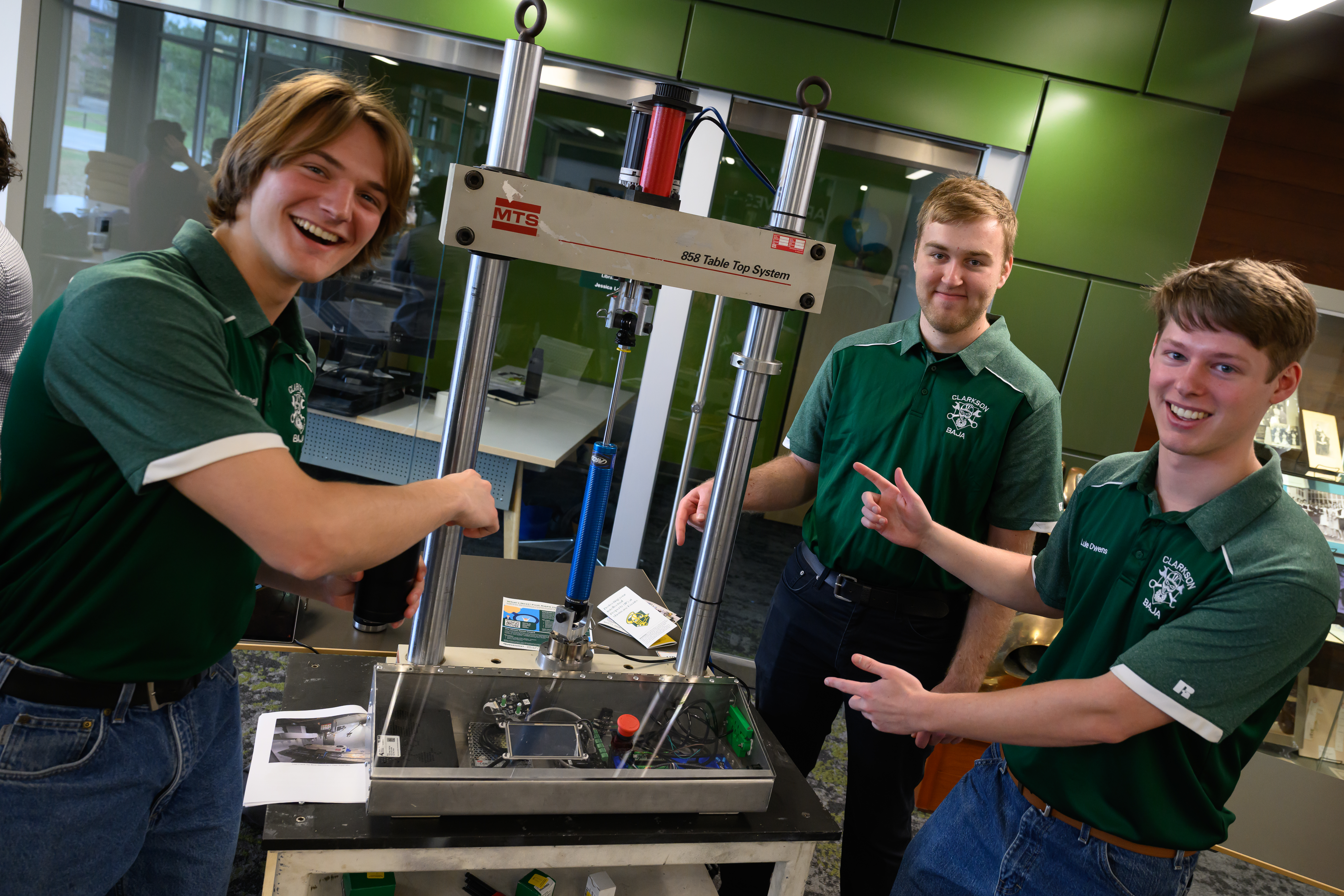 A photo of three students posing with an 858 Table Top System machine 
