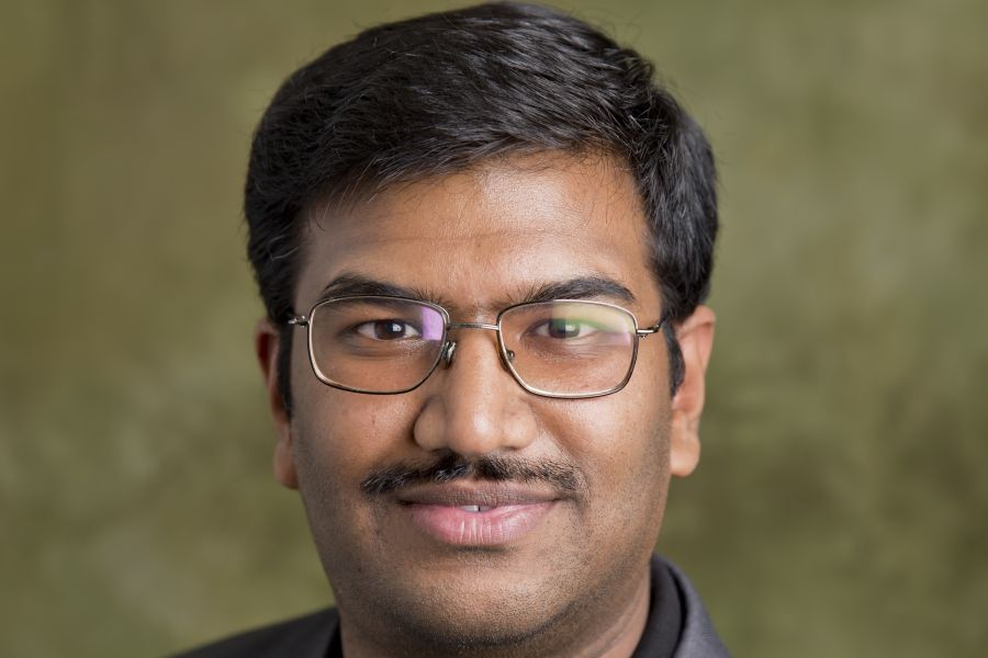 A professional headshot of Clarkson University Professor Mahesh Banavar, wearing glasses and a dark blazer against a soft green textured background.