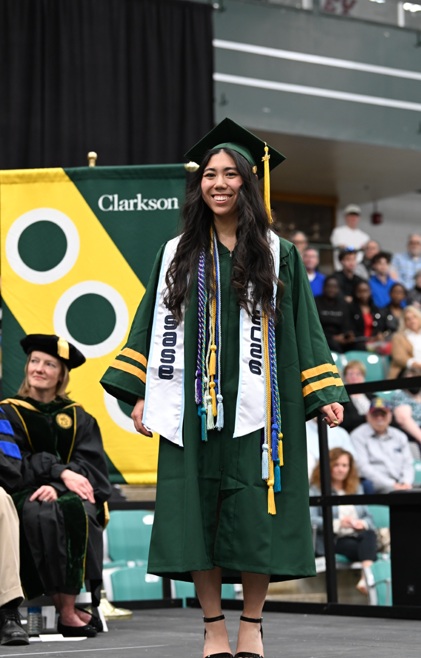 A student stands on stage in commencement regalia